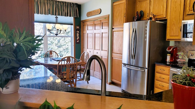 kitchen with appliances with stainless steel finishes, backsplash, an inviting chandelier, and dark stone countertops