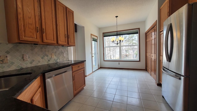 kitchen featuring light tile patterned floors, brown cabinetry, stainless steel appliances, a notable chandelier, and backsplash