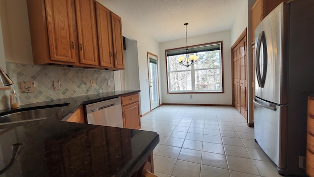 kitchen featuring brown cabinetry, an inviting chandelier, light tile patterned flooring, a sink, and appliances with stainless steel finishes