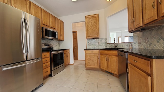 kitchen with light tile patterned floors, a sink, appliances with stainless steel finishes, dark countertops, and backsplash