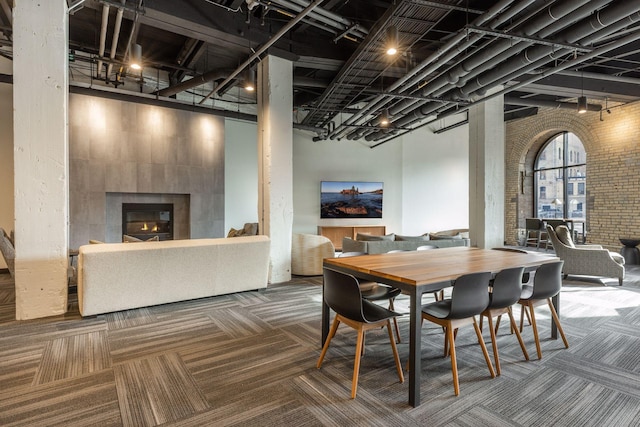 dining area with carpet floors, a towering ceiling, and a tiled fireplace