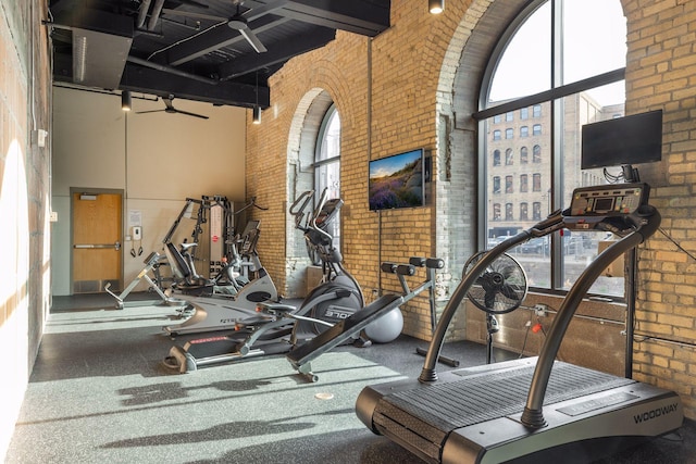 gym with a towering ceiling, ceiling fan, and brick wall