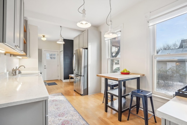 kitchen with sink, pendant lighting, light hardwood / wood-style flooring, gray cabinets, and stainless steel refrigerator