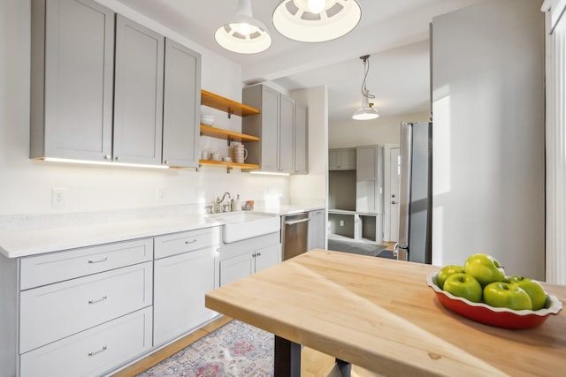 kitchen with butcher block counters, sink, stainless steel appliances, hanging light fixtures, and gray cabinets