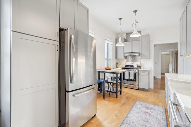 kitchen featuring gray cabinetry, hanging light fixtures, stainless steel appliances, light hardwood / wood-style flooring, and decorative backsplash