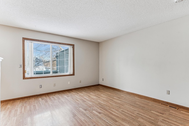 empty room with a textured ceiling and light hardwood / wood-style floors