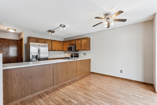 kitchen featuring light hardwood / wood-style floors, kitchen peninsula, stainless steel appliances, a textured ceiling, and sink