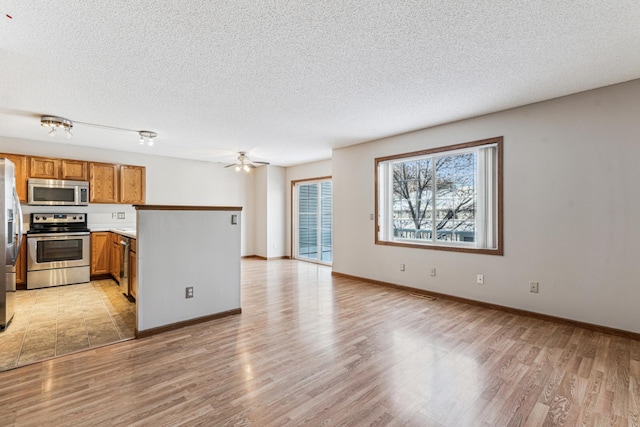 kitchen featuring a textured ceiling, ceiling fan, appliances with stainless steel finishes, and light hardwood / wood-style flooring