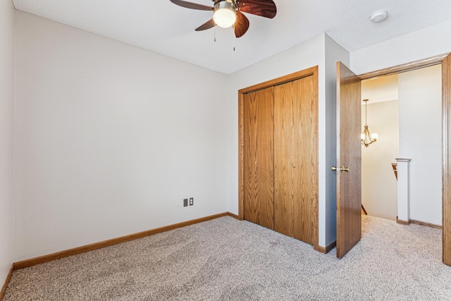 unfurnished bedroom with light colored carpet, a closet, and ceiling fan with notable chandelier