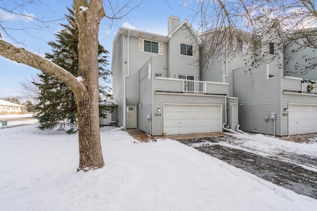 snow covered house featuring a balcony and a garage