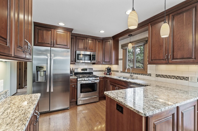 kitchen featuring light stone counters, stainless steel appliances, a sink, light wood-type flooring, and decorative light fixtures