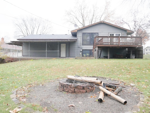 back of property featuring a fire pit, a sunroom, a wooden deck, and a lawn