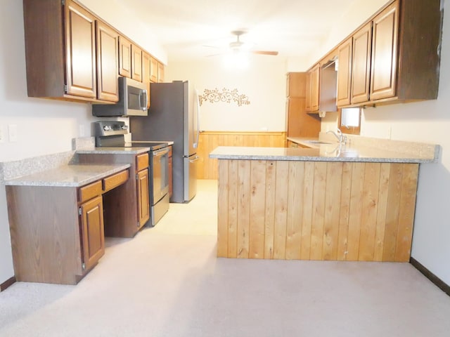 kitchen with wood walls, sink, ceiling fan, kitchen peninsula, and stainless steel appliances