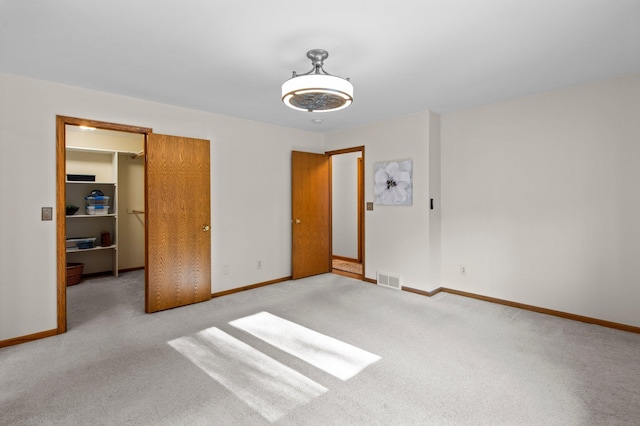 unfurnished bedroom featuring a walk in closet, light colored carpet, and a closet