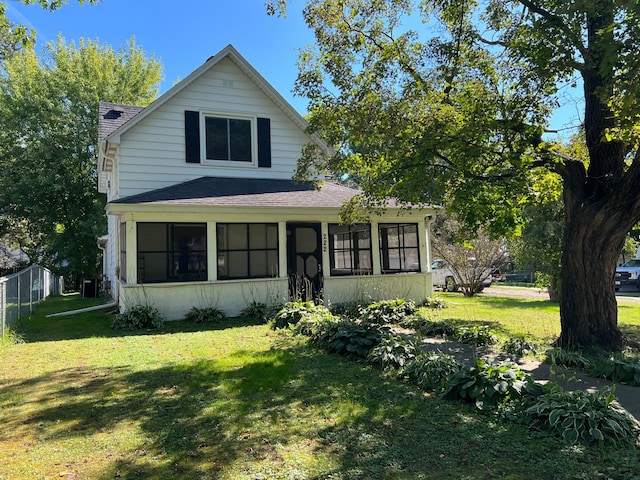 view of front facade featuring a front yard, a sunroom, roof with shingles, and fence