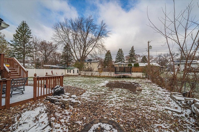 yard layered in snow featuring a trampoline, a shed, and a wooden deck