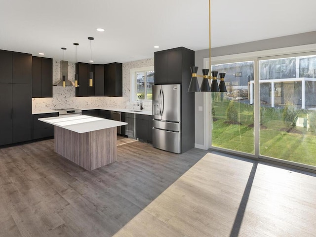 kitchen featuring stainless steel appliances, sink, wall chimney range hood, a center island, and hanging light fixtures