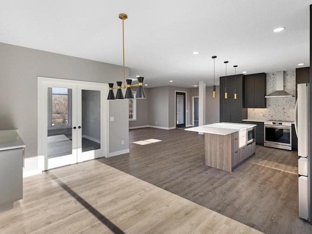 kitchen with backsplash, wall chimney exhaust hood, stainless steel appliances, light hardwood / wood-style flooring, and a center island