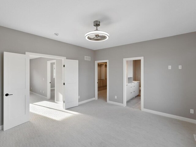 unfurnished bedroom featuring a walk in closet, light colored carpet, ensuite bath, and a closet