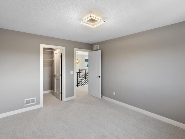 unfurnished bedroom featuring a walk in closet, a closet, light colored carpet, and a textured ceiling