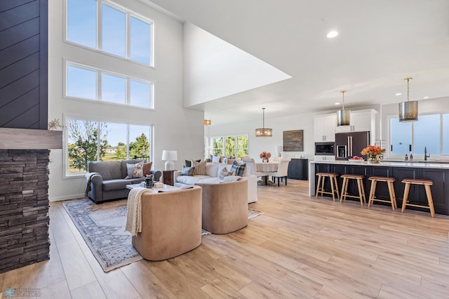 living room featuring a towering ceiling, sink, light hardwood / wood-style floors, and a wealth of natural light