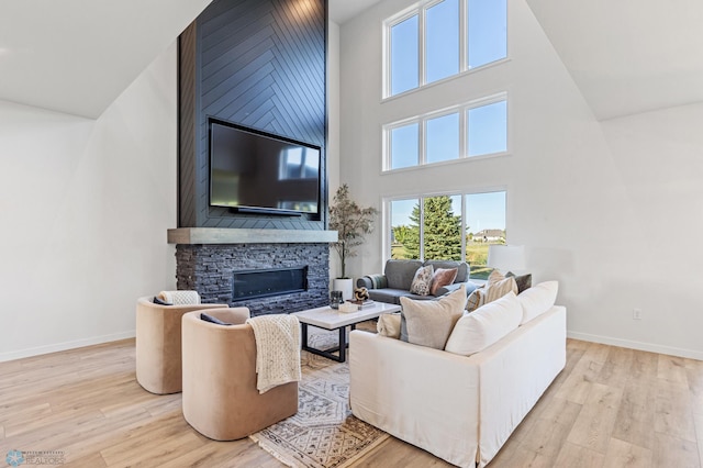 living room featuring a stone fireplace, light hardwood / wood-style flooring, and a towering ceiling