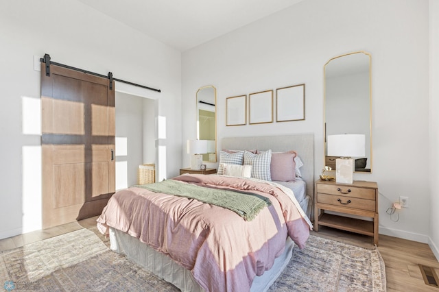 bedroom with a barn door and light wood-type flooring