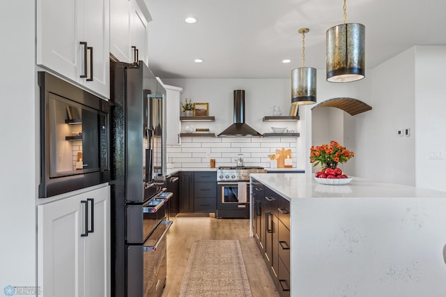 kitchen with pendant lighting, white cabinets, wall chimney exhaust hood, black appliances, and light hardwood / wood-style flooring