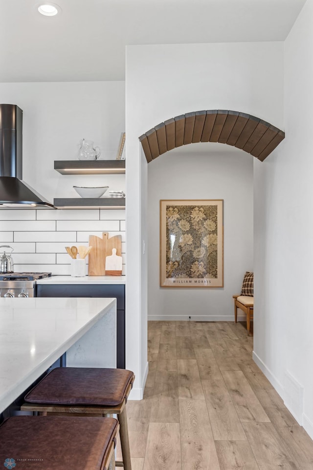 interior space featuring stove, decorative backsplash, light hardwood / wood-style floors, and wall chimney exhaust hood