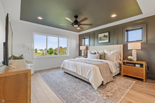 bedroom with ceiling fan, a tray ceiling, and light wood-type flooring