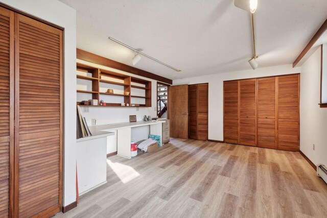 interior space with light hardwood / wood-style floors, built in desk, rail lighting, and a baseboard heating unit