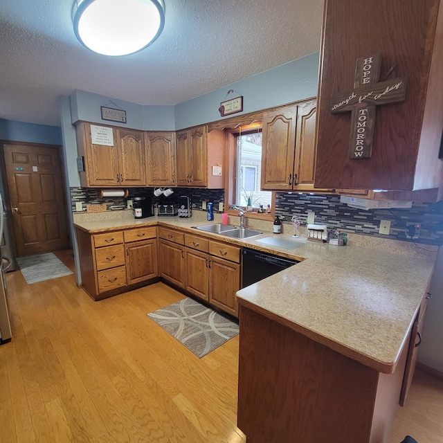 kitchen with black dishwasher, light countertops, brown cabinetry, a sink, and a peninsula