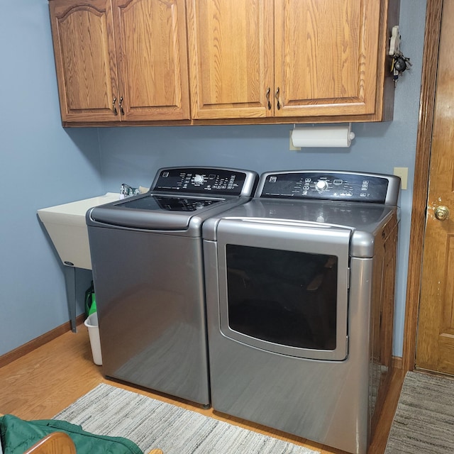 laundry room featuring separate washer and dryer, light wood-type flooring, cabinet space, and baseboards