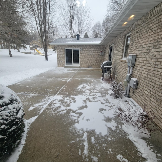 view of snow covered exterior featuring brick siding and a playground