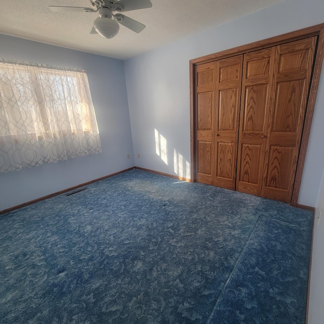 unfurnished bedroom featuring a textured ceiling, dark colored carpet, visible vents, and baseboards