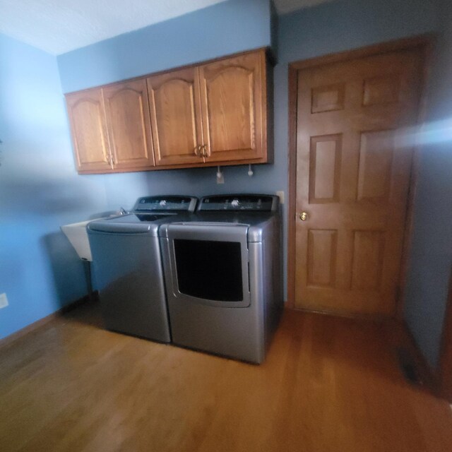 clothes washing area with cabinet space, washing machine and dryer, and light wood-style floors