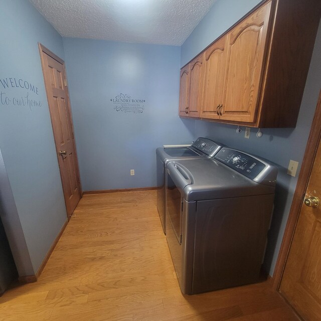 laundry room with cabinet space, baseboards, a textured ceiling, light wood-style floors, and washing machine and dryer