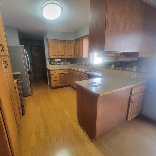 kitchen with a peninsula, a sink, stainless steel electric stove, light wood finished floors, and brown cabinetry