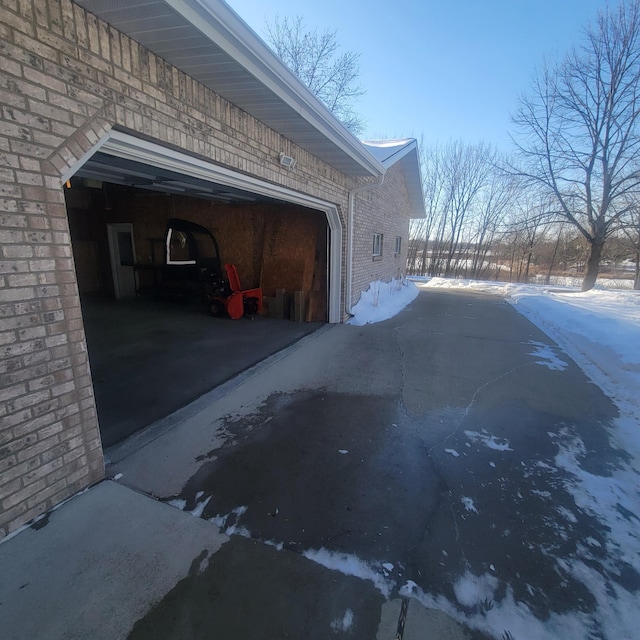 view of snowy exterior with a garage, aphalt driveway, and brick siding