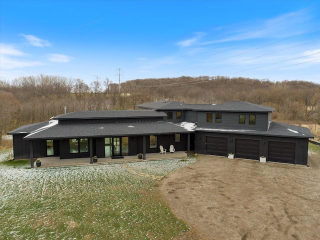 back of house featuring an attached garage, roof with shingles, and dirt driveway