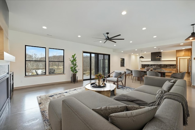 living room featuring finished concrete flooring, baseboards, ceiling fan, recessed lighting, and a fireplace