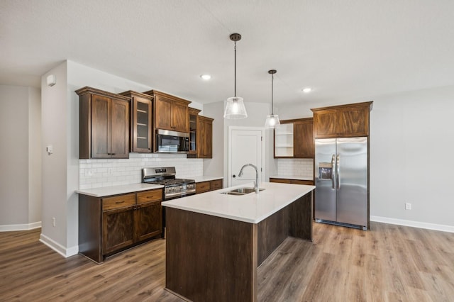 kitchen with a kitchen island with sink, a sink, light countertops, appliances with stainless steel finishes, and hanging light fixtures