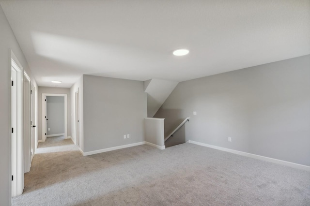 additional living space featuring baseboards and light colored carpet