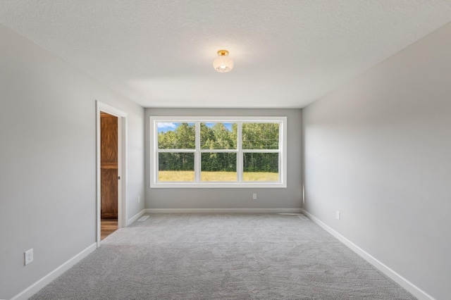 empty room featuring light carpet, a textured ceiling, and baseboards