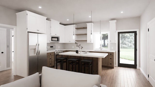 kitchen featuring sink, decorative light fixtures, appliances with stainless steel finishes, hardwood / wood-style floors, and a kitchen island with sink