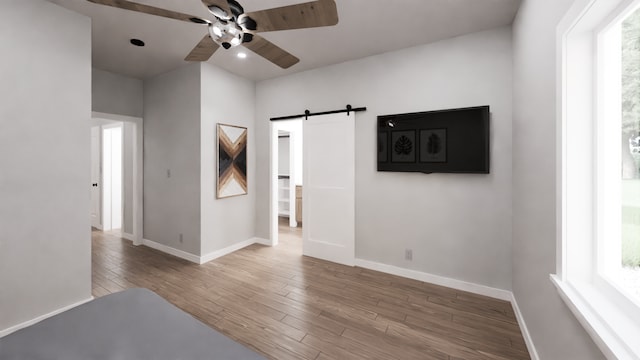 unfurnished room with light hardwood / wood-style flooring, a barn door, and ceiling fan