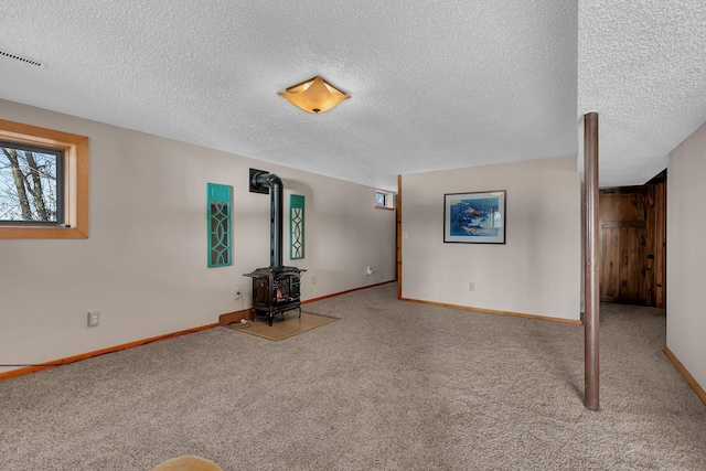 unfurnished living room featuring visible vents, a textured ceiling, carpet flooring, baseboards, and a wood stove