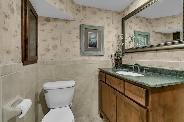 bathroom featuring vanity, wallpapered walls, wainscoting, tile walls, and toilet