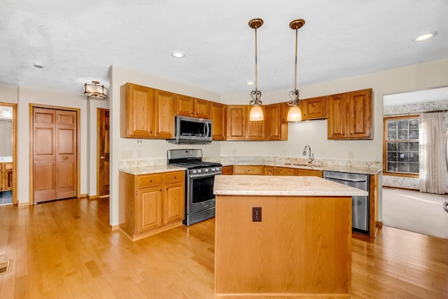 kitchen with appliances with stainless steel finishes, light hardwood / wood-style floors, a kitchen island, and hanging light fixtures