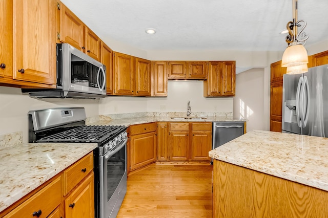 kitchen featuring light stone countertops, sink, pendant lighting, appliances with stainless steel finishes, and light wood-type flooring